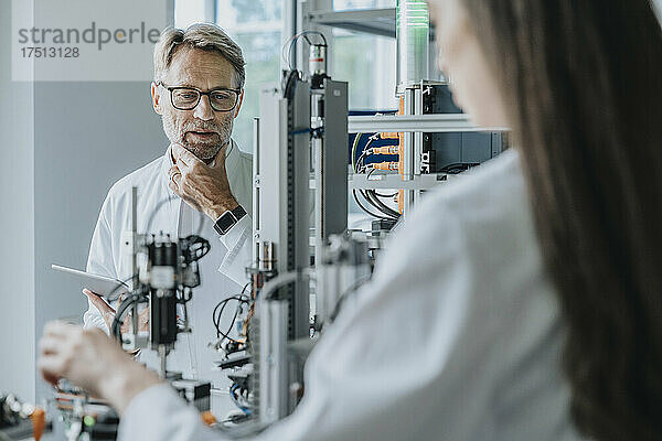 Nachdenklicher männlicher Wissenschaftler blickt auf Maschinen  während er mit einer Kollegin im Labor arbeitet