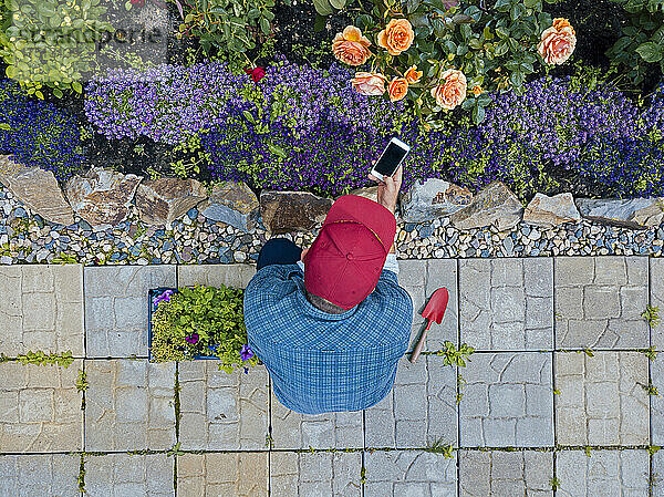 Mann kauert im Garten und fotografiert Blumen mit Smartphone