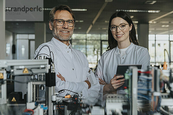 Lächelnde männliche und weibliche Wissenschaftler stehen neben Maschinen im Labor