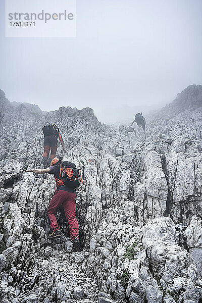 Männliche Wanderer klettern bei nebligem Wetter auf einen felsigen Berg gegen den Himmel  Bergamasker Alpen  Italien