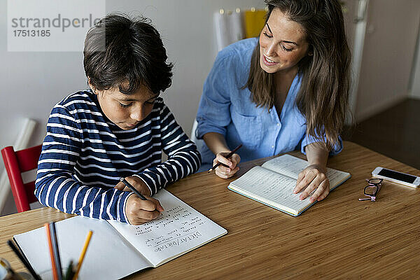Junge Frau hilft Jungen beim Schreiben von Hausaufgaben auf dem heimischen Tisch