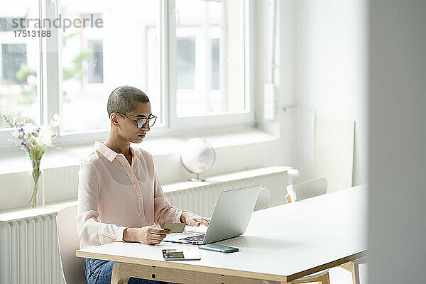 Geschäftsfrau hält Kreditkarte in der Hand und benutzt Laptop am Schreibtisch im Loft-Büro