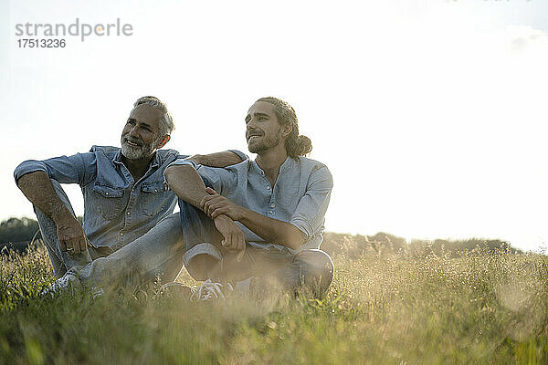 Reifer Vater mit erwachsenem Sohn sitzt auf einer Wiese auf dem Land