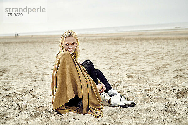 Niederlande  Porträt einer blonden jungen Frau  die am Strand sitzt