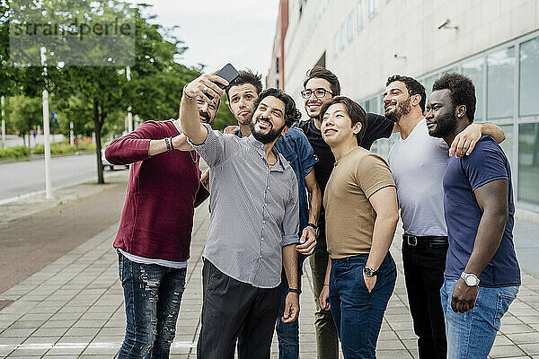 Mann macht Selfie mit männlichen Freunden  während er auf dem Fußweg in der Stadt steht