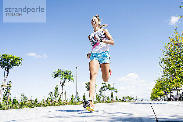 Mittlere erwachsene Frau joggt auf der Straße vor blauem Himmel