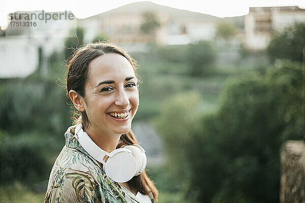 Lächelnde Frau mit Kopfhörern steht im öffentlichen Park