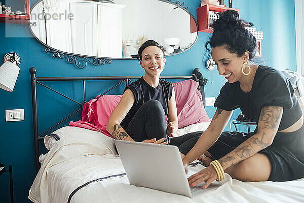 Lächelnde Frau benutzt Laptop ihres Partners im Schlafzimmer
