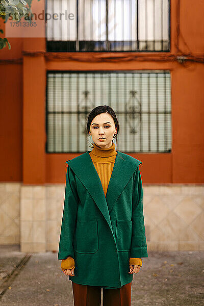 Junge Frau in grüner Jacke steht vor einem Gebäude in der Stadt
