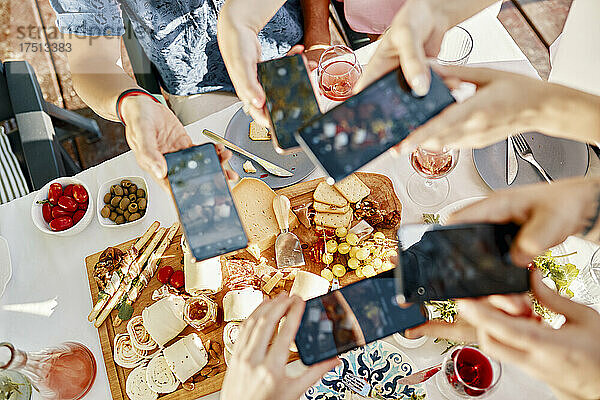 Freunde essen mit einer Käseplatte zu Abend und machen Smartphone-Fotos