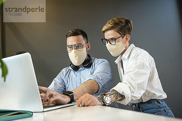 Männliche und weibliche Kollegen planen Strategie  während sie während einer Pandemie am Laptop am Schreibtisch im Büro diskutieren