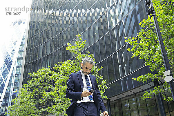 Geschäftsmann schreibt SMS über Mobiltelefon vor Bürogebäude in der Stadt