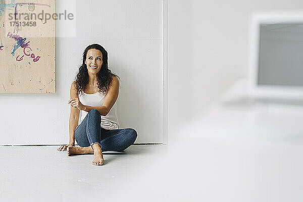 Nachdenkliche Frau schaut weg  während sie im Dachgeschoss auf dem Boden an der Wand sitzt