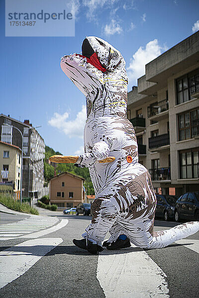 Großer Spielzeugdinosaurier mit Brot läuft auf Zebrastreifen gegen den Himmel in der Stadt