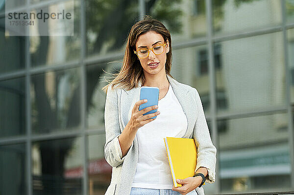Geschäftsfrau schreibt Textnachrichten per Smartphone vor dem Bürogebäude