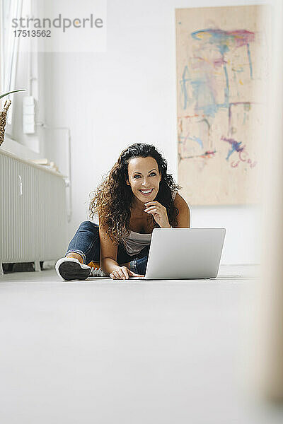 Lächelnde Frau mittleren Alters  die zu Hause einen Laptop auf dem Boden benutzt
