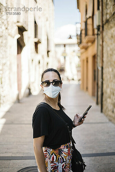 Frau trägt Schutzkleidung und benutzt Smartphone in Gasse