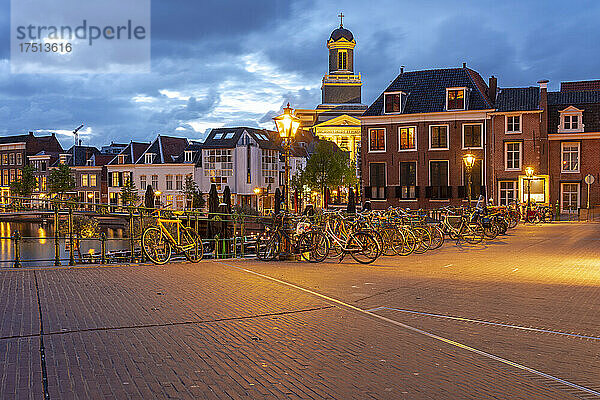 Niederlande  Südholland  Leiden  Fahrräder  die in der Abenddämmerung entlang der beleuchteten Altstadtstraße geparkt sind
