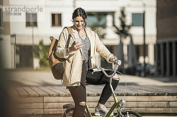 Studentin benutzt Mobiltelefon  während sie an sonnigen Tagen auf dem Fahrrad in der Stadt sitzt
