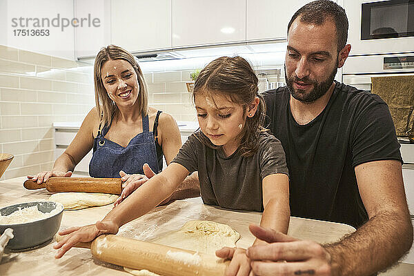 Familie knetet Pizzateig mit Nudelholz auf dem Tisch in der Küche