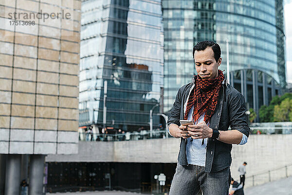 Trendiger Mann  der Textnachrichten per Smartphone sendet  während er in der Stadt steht
