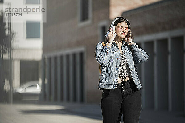 Lächelnde Pendlerin hört Musik über Kopfhörer  während sie auf der Straße in der Stadt läuft