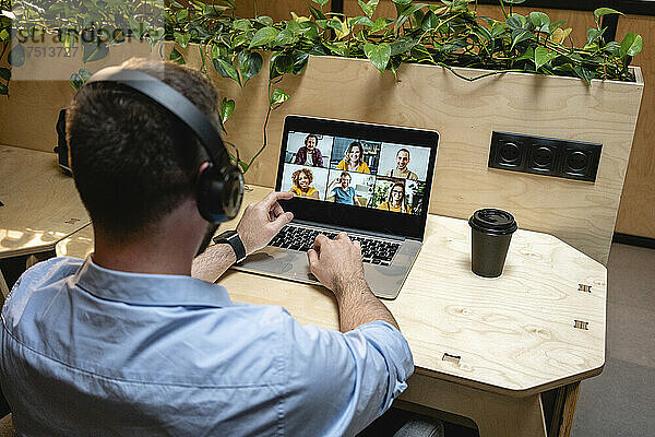 Männlicher Unternehmer führt Videoanruf mit Kollegen über Laptop  während er am Schreibtisch im Kreativbüro sitzt