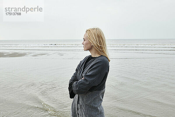 Niederlande  blonde junge Frau steht am Strand und blickt in die Ferne
