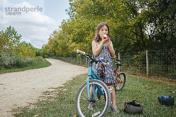 Ein kleines Mädchen auf dem Fahrrad macht im Sommer eine Pause  um Apfel zu essen