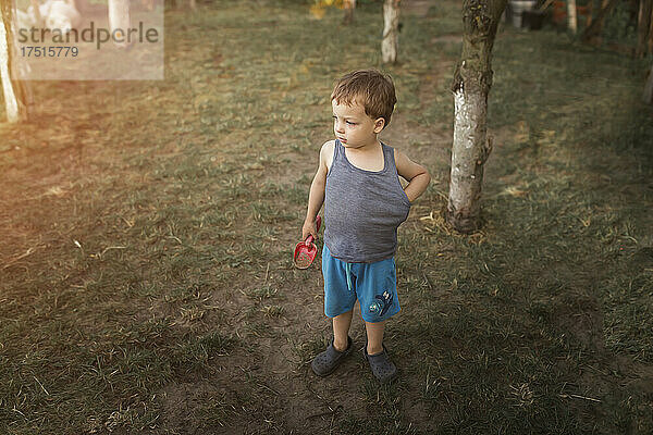 Kleiner blonder Junge steht in blauen Shorts im Garten und hält sich fest