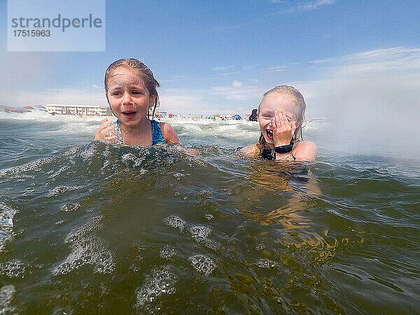 Zwei Mädchen lachen zusammen  während sie im Sommer im Meer Wellen springen