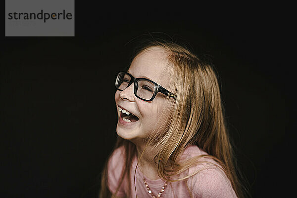 Porträt eines kleinen Mädchens  das vor schwarzem Hintergrund lacht