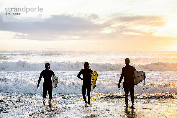 Surfende Jungs gehen bei Sonnenaufgang ins Wasser  Wellen im Hintergrund