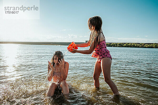Junges Mädchen bespritzt große Schwester mit Wasser im See
