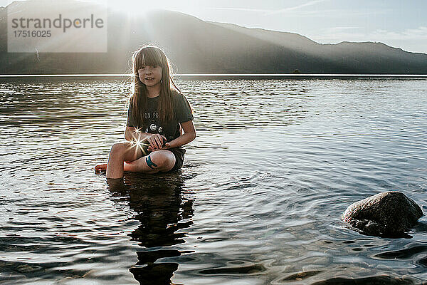 Junges Mädchen sitzt an einem sonnigen Tag auf einem Felsen in einem See
