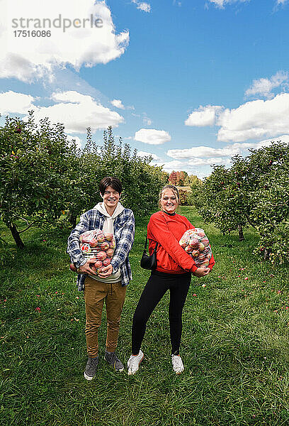 Fröhliche Teenager halten Säcke mit frisch gepflückten Äpfeln in einem Obstgarten.
