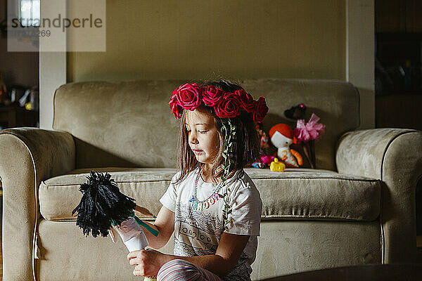 Ein kleines Mädchen mit einem Blumenkranz auf dem Kopf spielt zu Hause mit Puppen