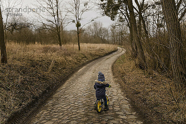 Kleinkind fährt mit warmer Mütze Fahrrad auf Landstraße