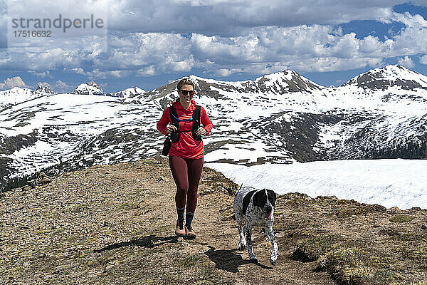 Lächelnde Frau wandert mit Hund gegen schneebedeckten Berg