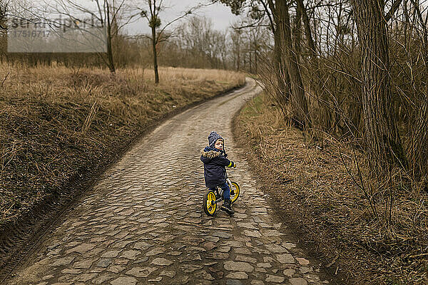 Kleinkind fährt mit warmer Mütze Fahrrad auf Landstraße