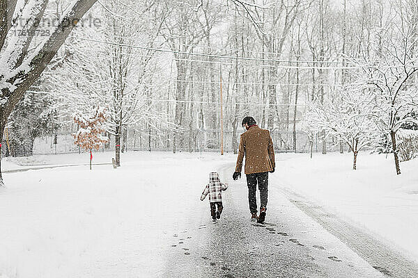 Vater und Kleinkind gehen an einem verschneiten Tag in einem Viertel die Straße entlang