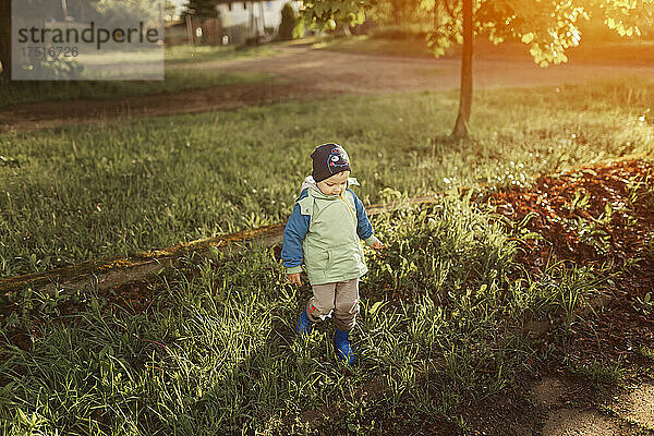Kleiner Junge läuft in blauen Gummistiefeln auf Gras im Park