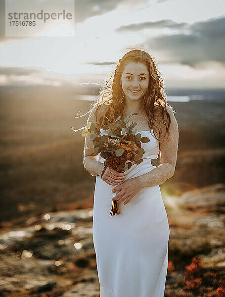 Braut mit Blumen bei Sonnenuntergang lächelt und grinst vor Glück