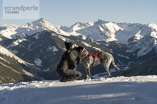 Wanderin küsst im Urlaub Hund auf schneebedecktem Berg