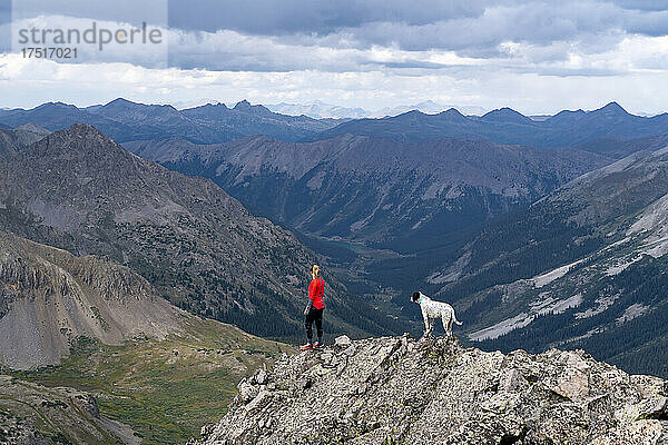 Wanderin blickt mit Hund auf Bergkette vor bewölktem Himmel