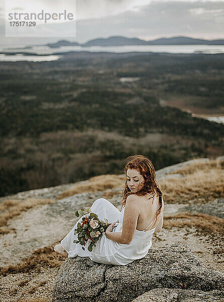 Braut im Hochzeitskleid sitzt auf einem Berg mit weitem Ausblick
