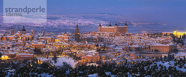 Altstadt mit Burg auf einem verschneiten Hügel bei Sonnenuntergang und beleuchteten Straßen