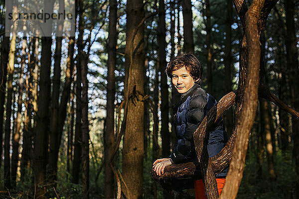 Ein lächelnder Junge lehnt an einem Ast im goldenen Wald