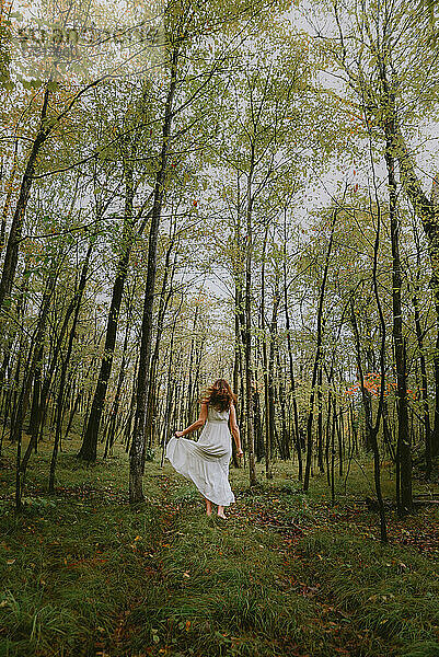 Frau in weißem Kleid rennt durch eine Lichtung im Wald.