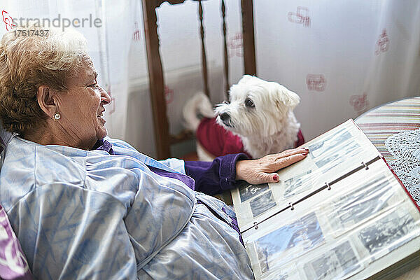 Ältere Frau schaut sich mit ihrem Hund ein Album mit alten Fotos an